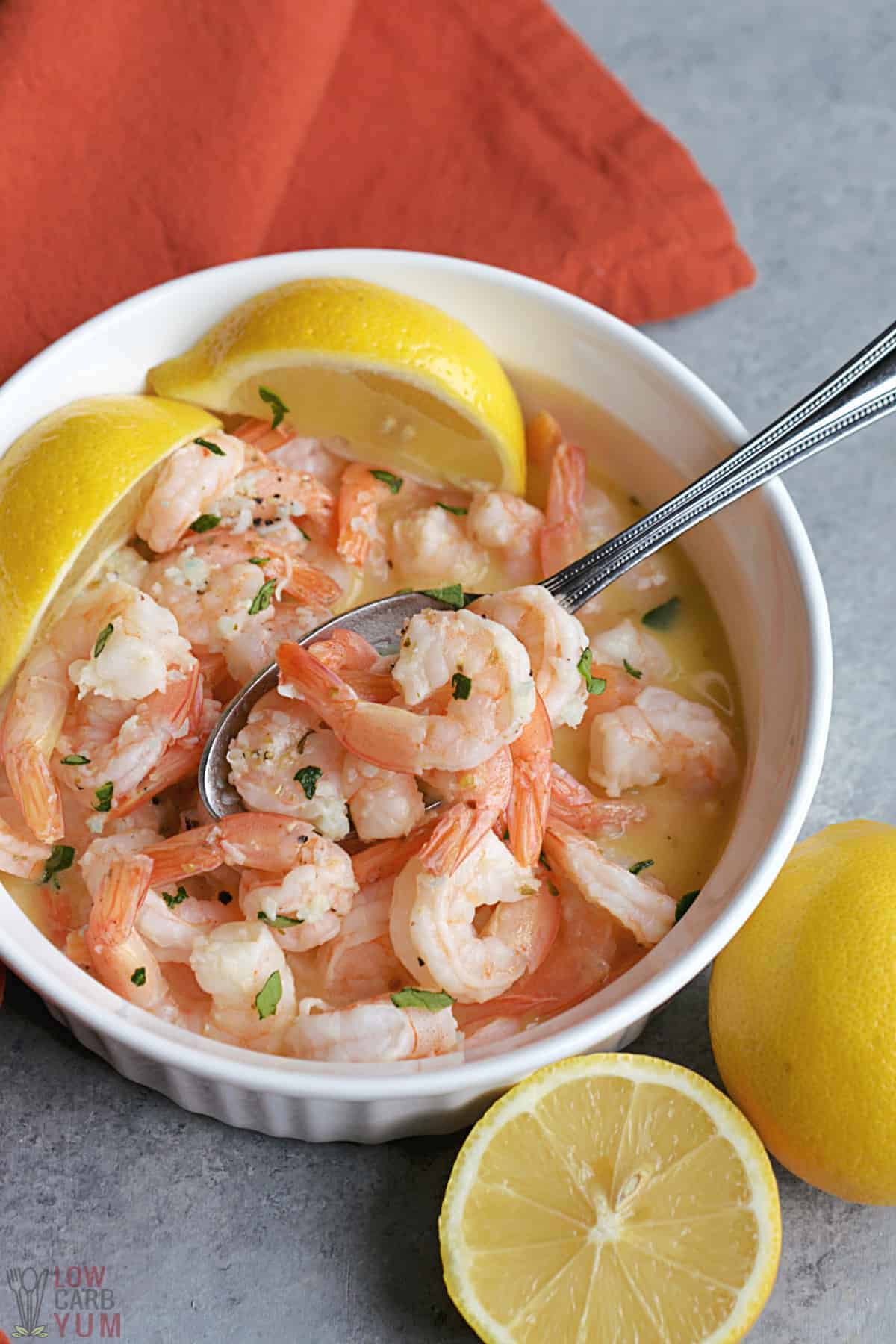 crock pot shrimp scampi in bowl with lemon wedges and spoon.