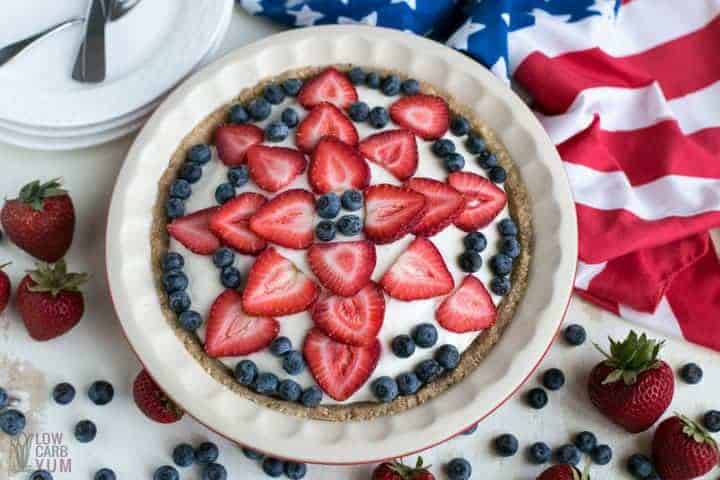 Finished keto low carb no bake cheesecake in pie pan topped with blueberries and sliced strawberries