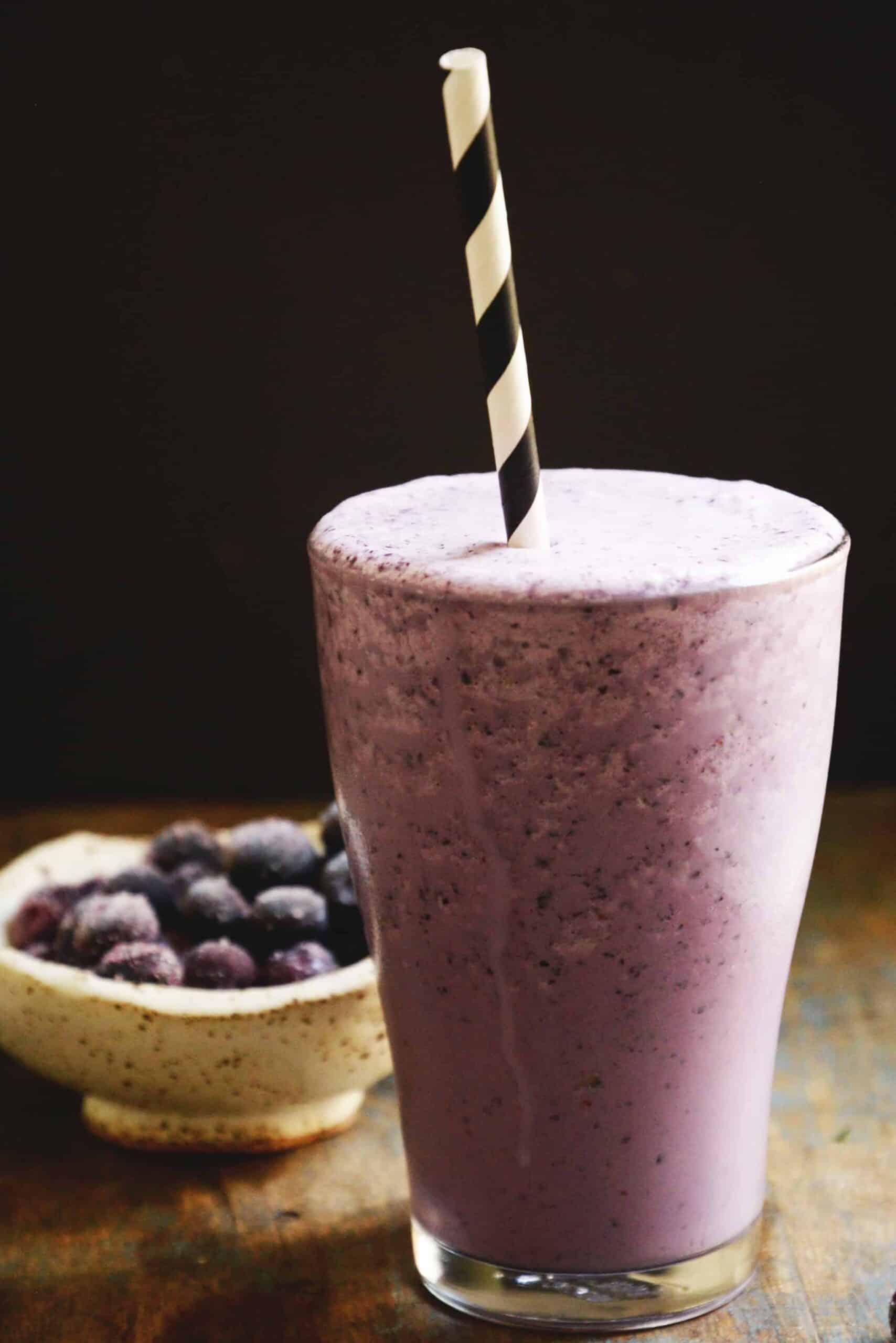 low carb blueberry smoothie in frosted glass with black and white striped straw