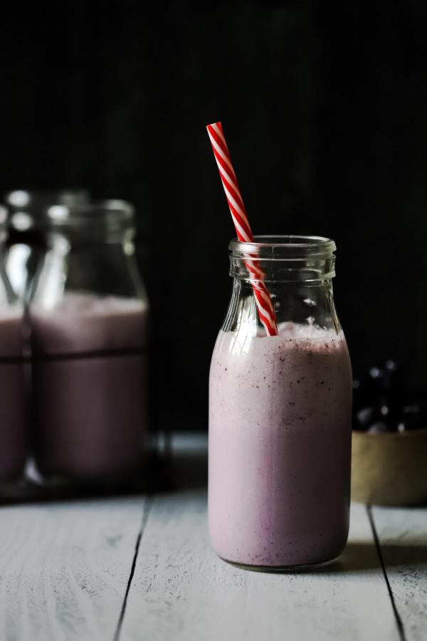 low carb blueberry smoothie in glass milk bottle with red and white striped straw
