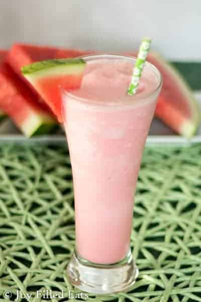 watermelon smoothie in tall glass with watermelon wedge on rim