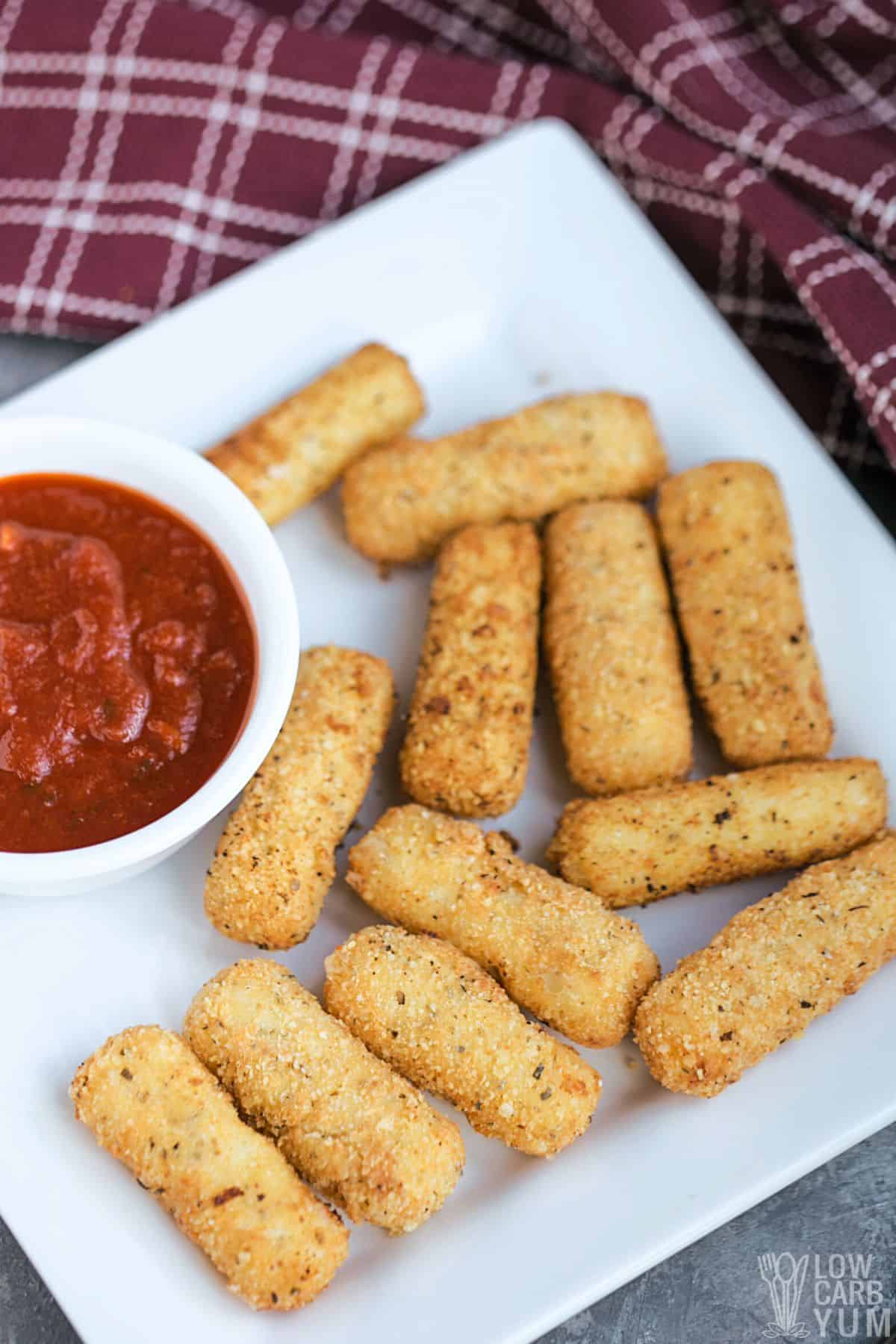 keto mozzarella sticks on square white plate with tomato sauce.