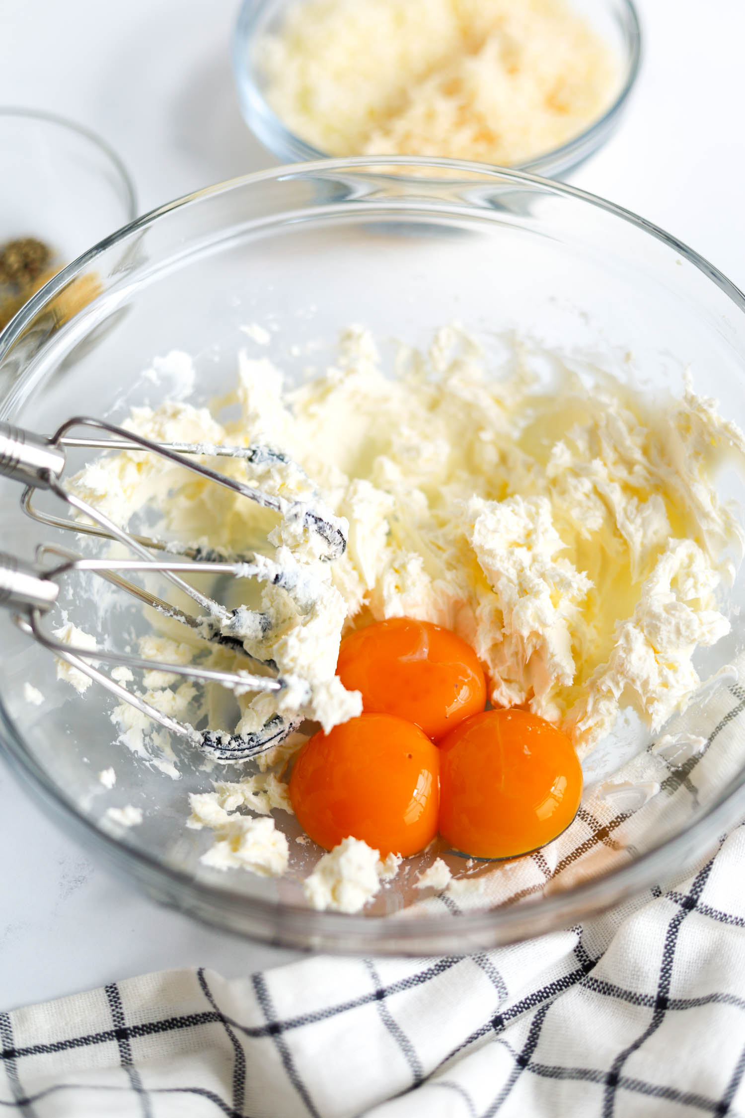 adding egg yolks to cream cheese in a glass bowl 