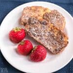 low-carb keto french toast slices with powdered sweetener on white plate with powdered sweetener and strawberries.