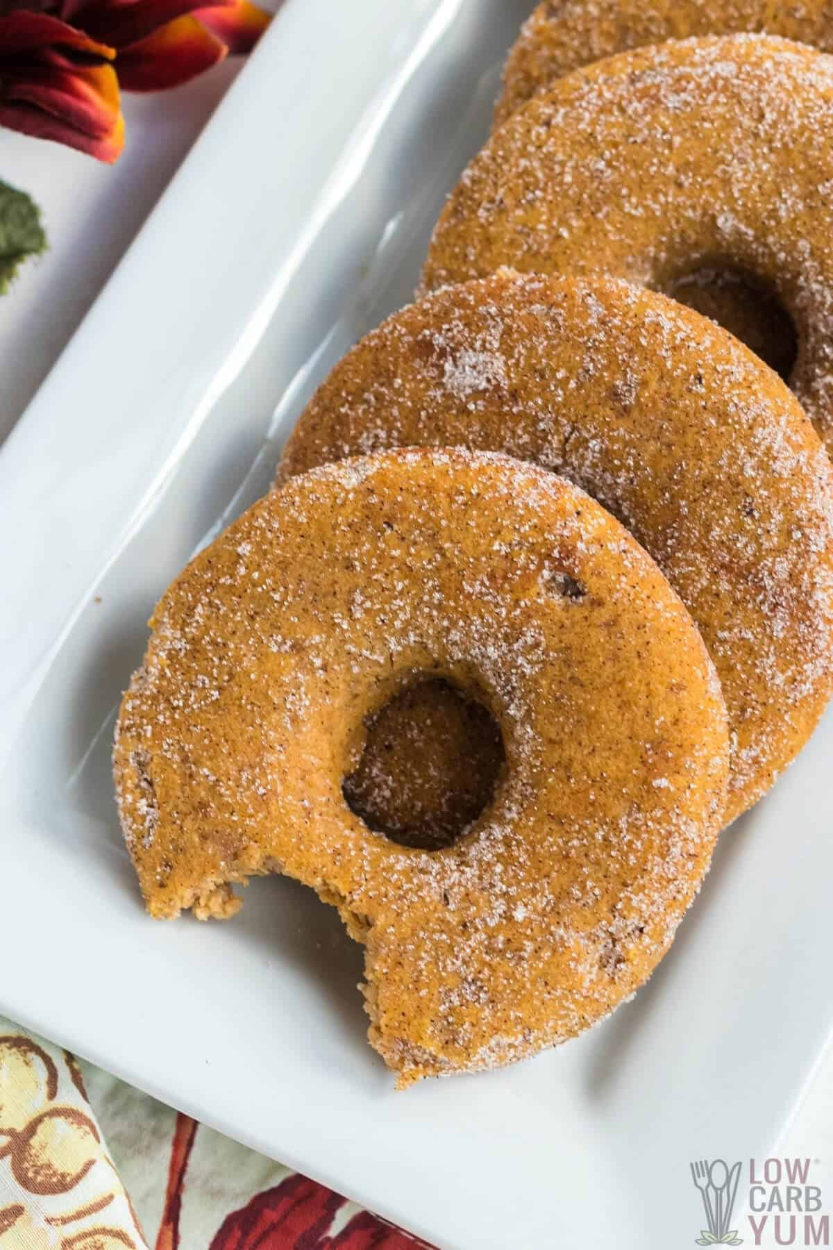 keto pumpkin donuts on white platter one with a bite