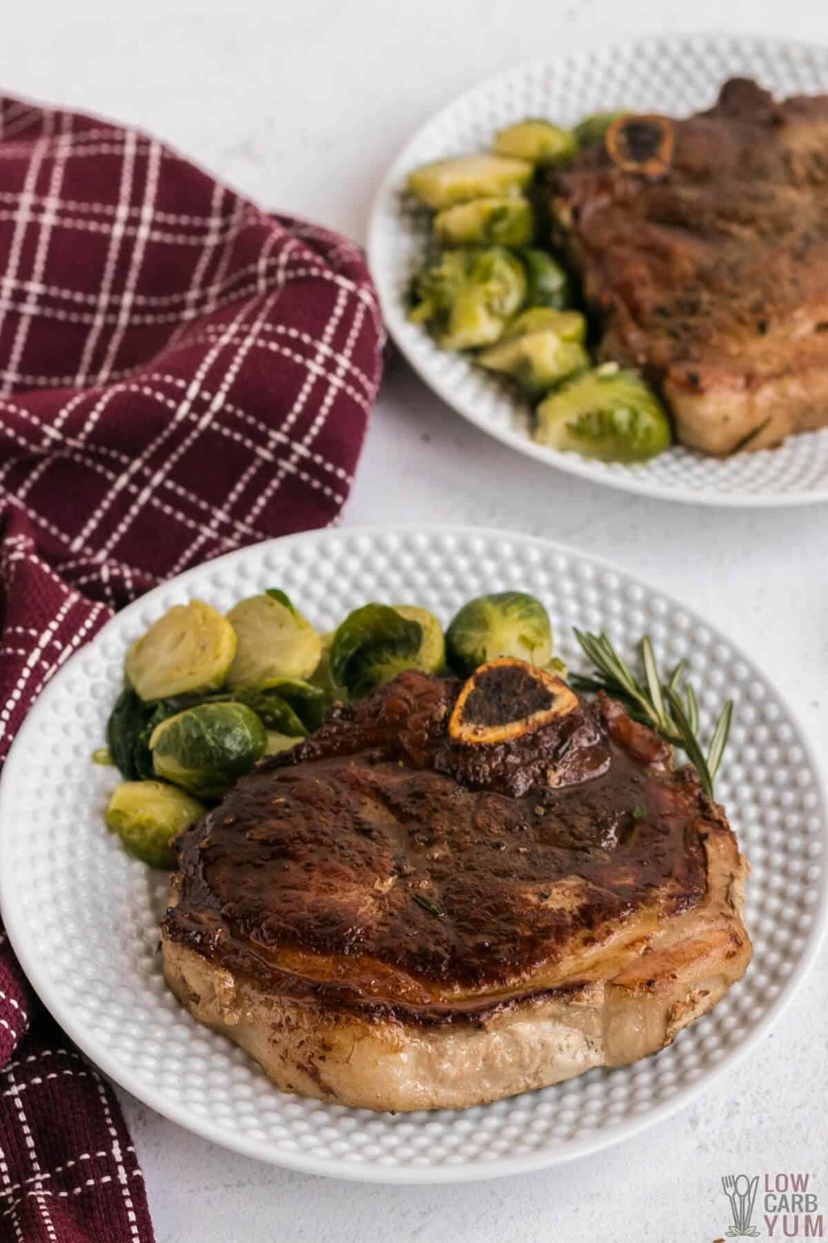 cooked berkshire pork chops on plates are next to keto brussel sprouts