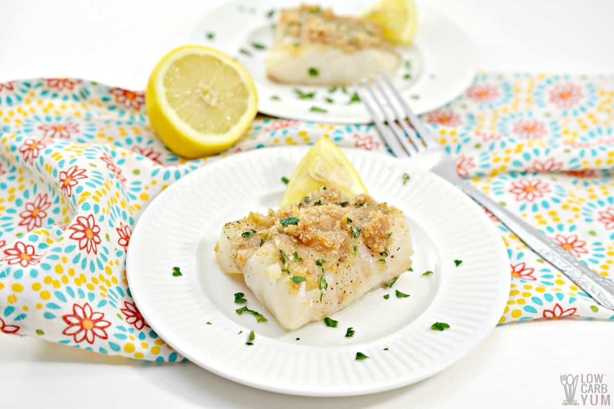 keto baked cod fillet on plate with chopped parsley and a slice of lemon 