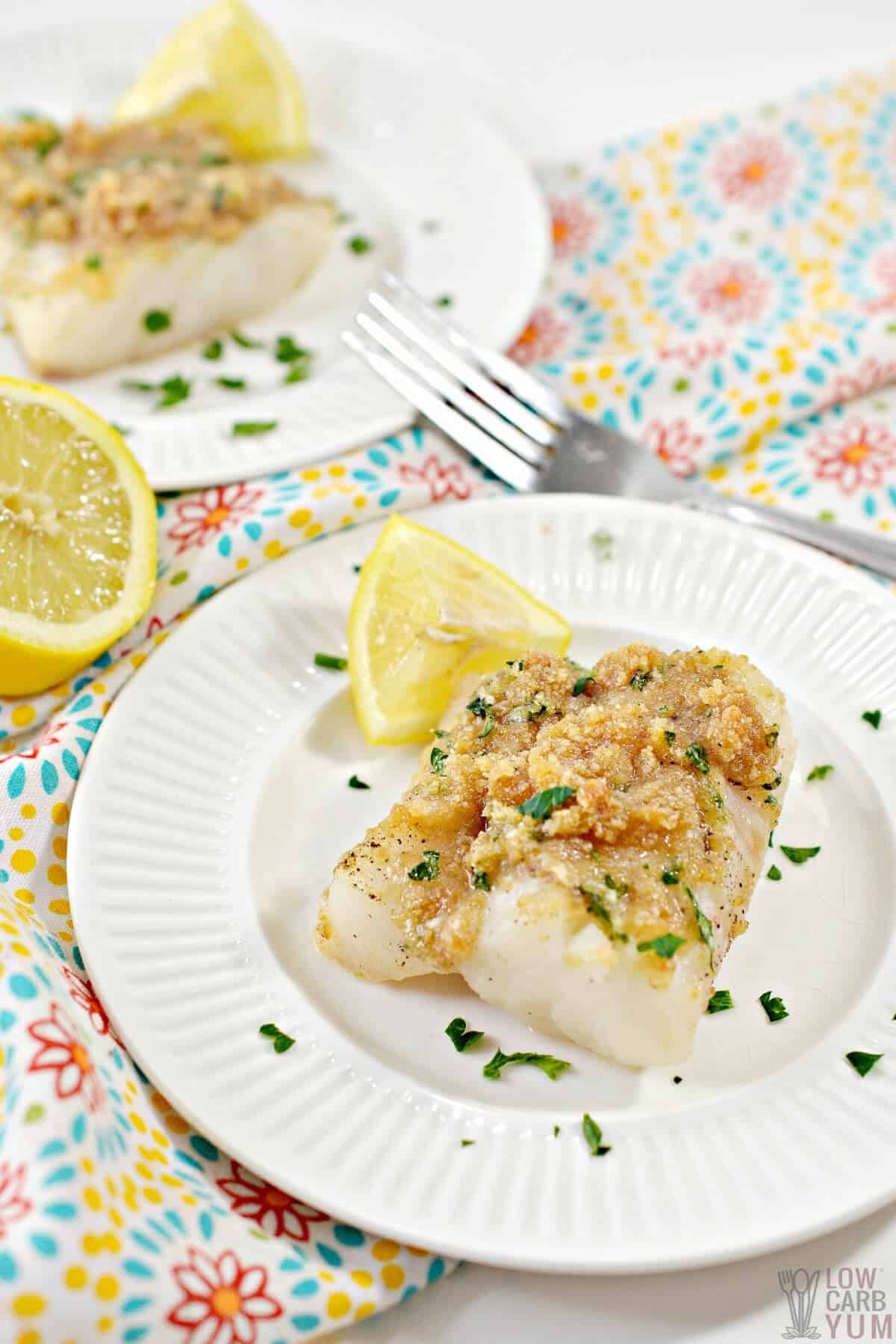 baked cod with keto breadcrumbs on white plates with lemon slices