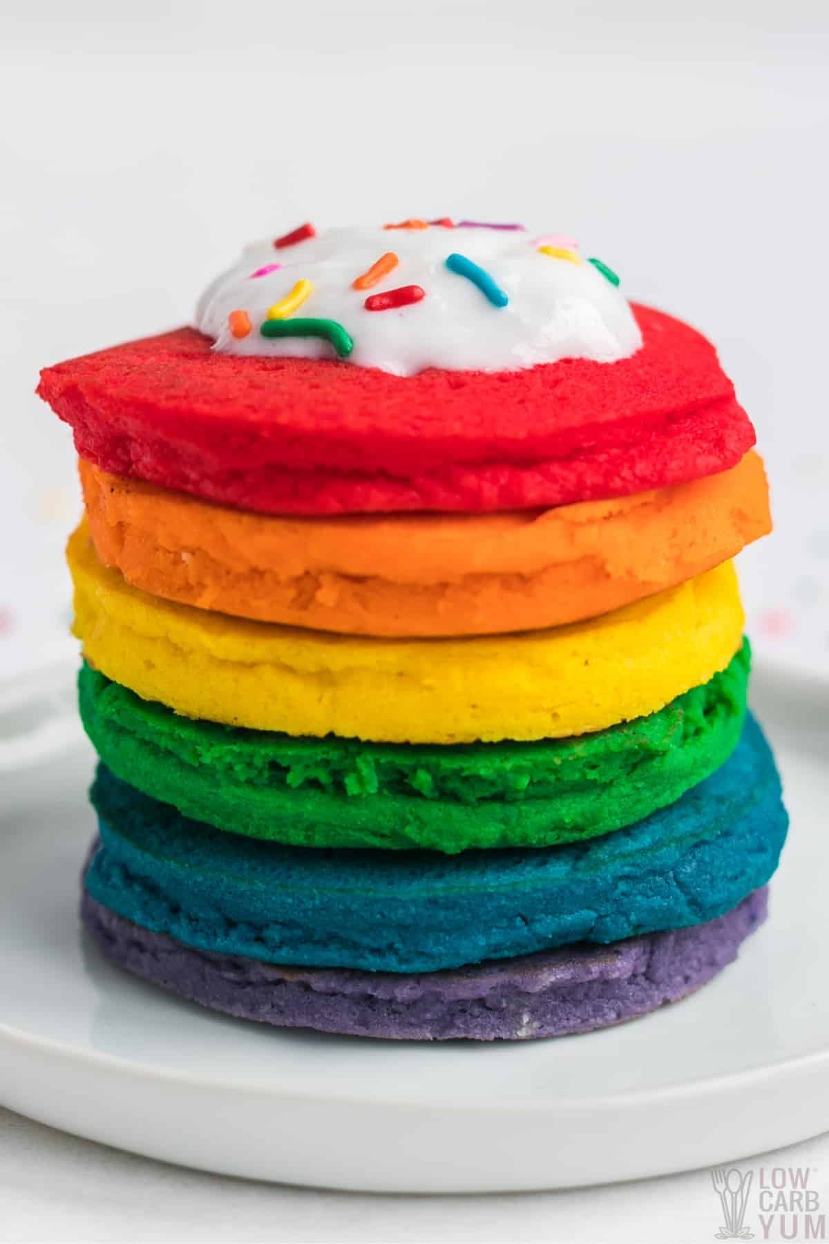 rainbow pancakes in stack with whipped cream and sprinkles on top