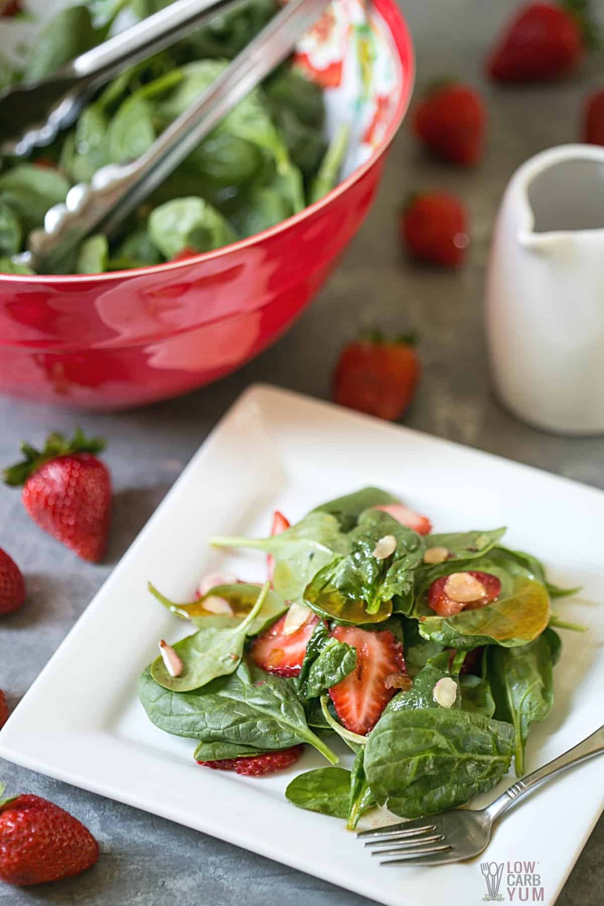 strawberry spinach salad on white square plate with vinaigrette dressing