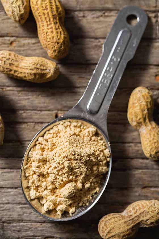 peanut flour in measuring spoon with peanuts