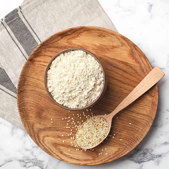 sesame seed flour on wood platter with seeds