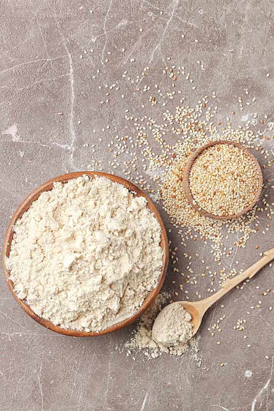 sesame seed flour in bowl with seeds in bowl and spoon