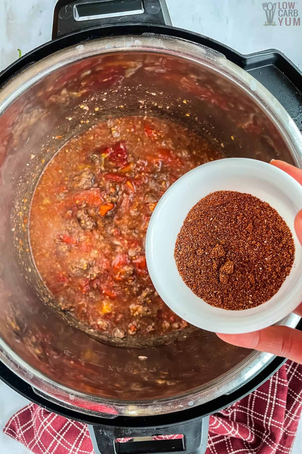 adding chili seasoning to pot of chili