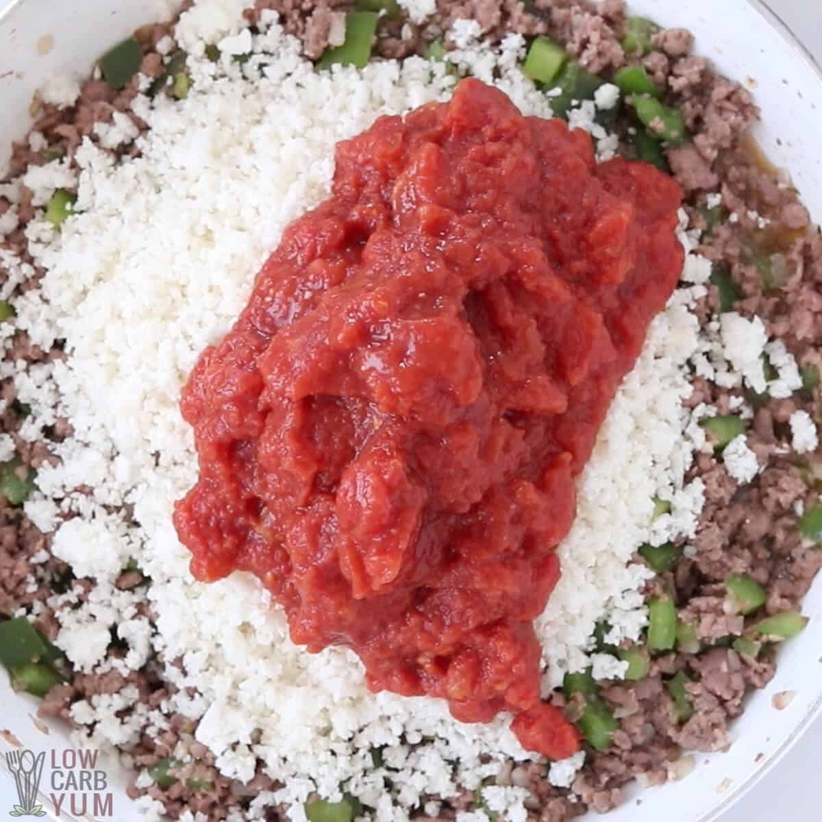 adding cauliflower rice and canned tomatoes to the meat mixture
