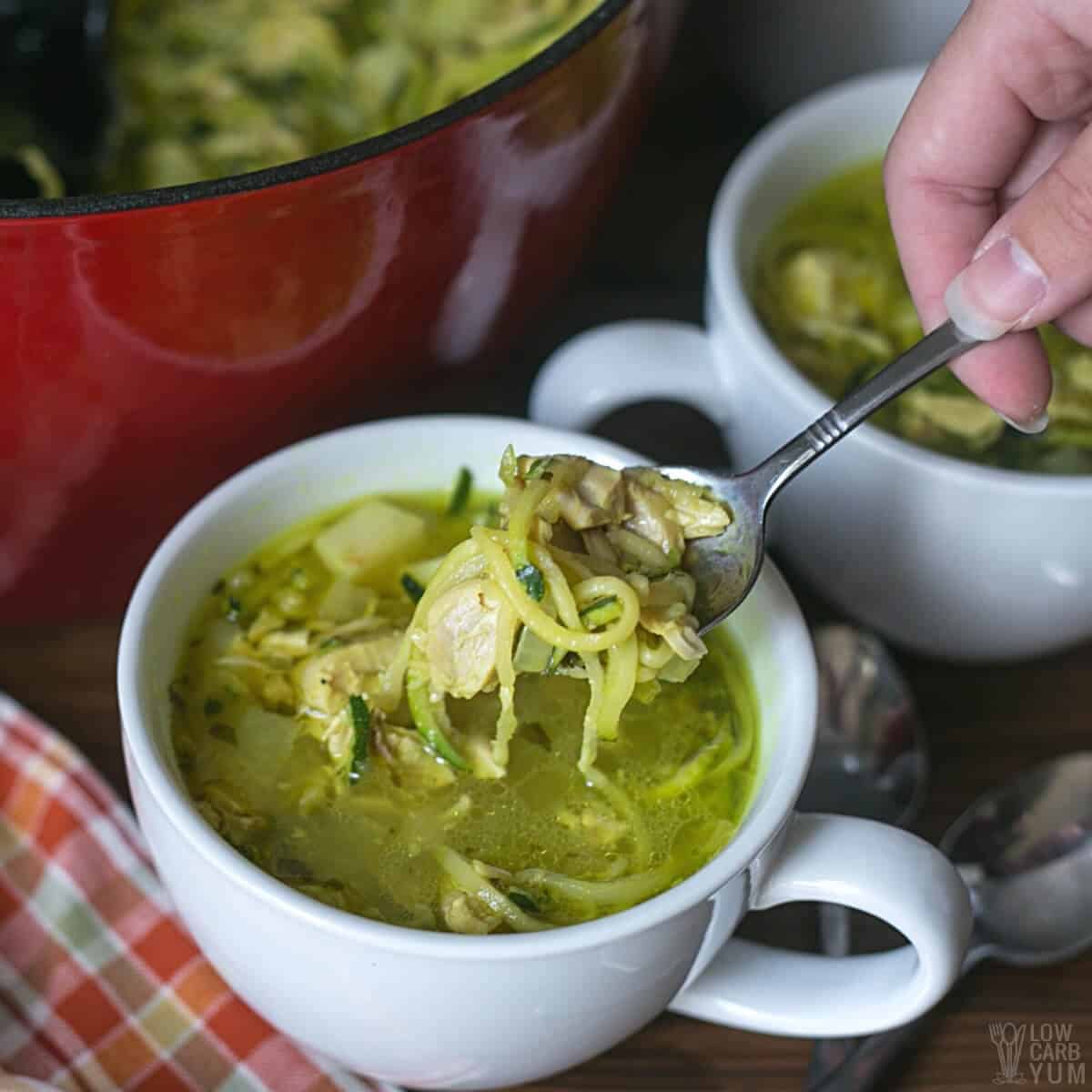 chicken zoodle soup on spoon over large white mug