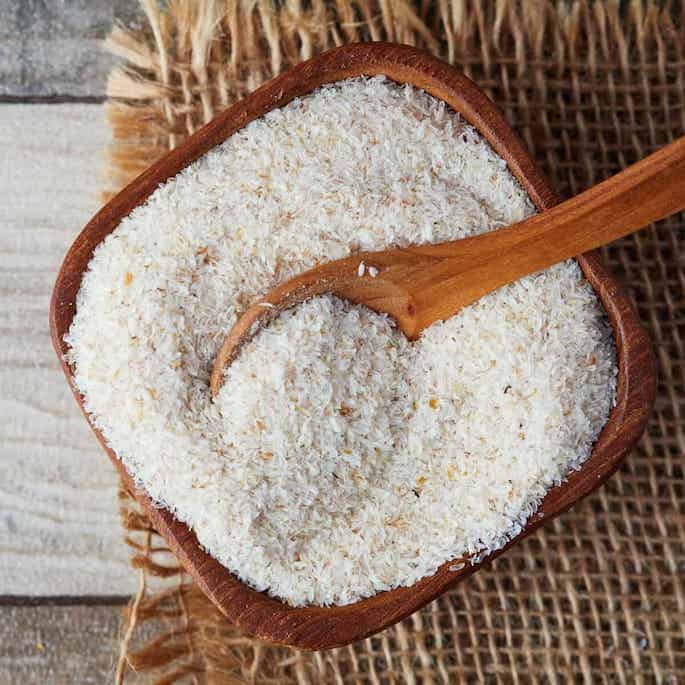 psyllium husks in square wooden bowl with spoon.