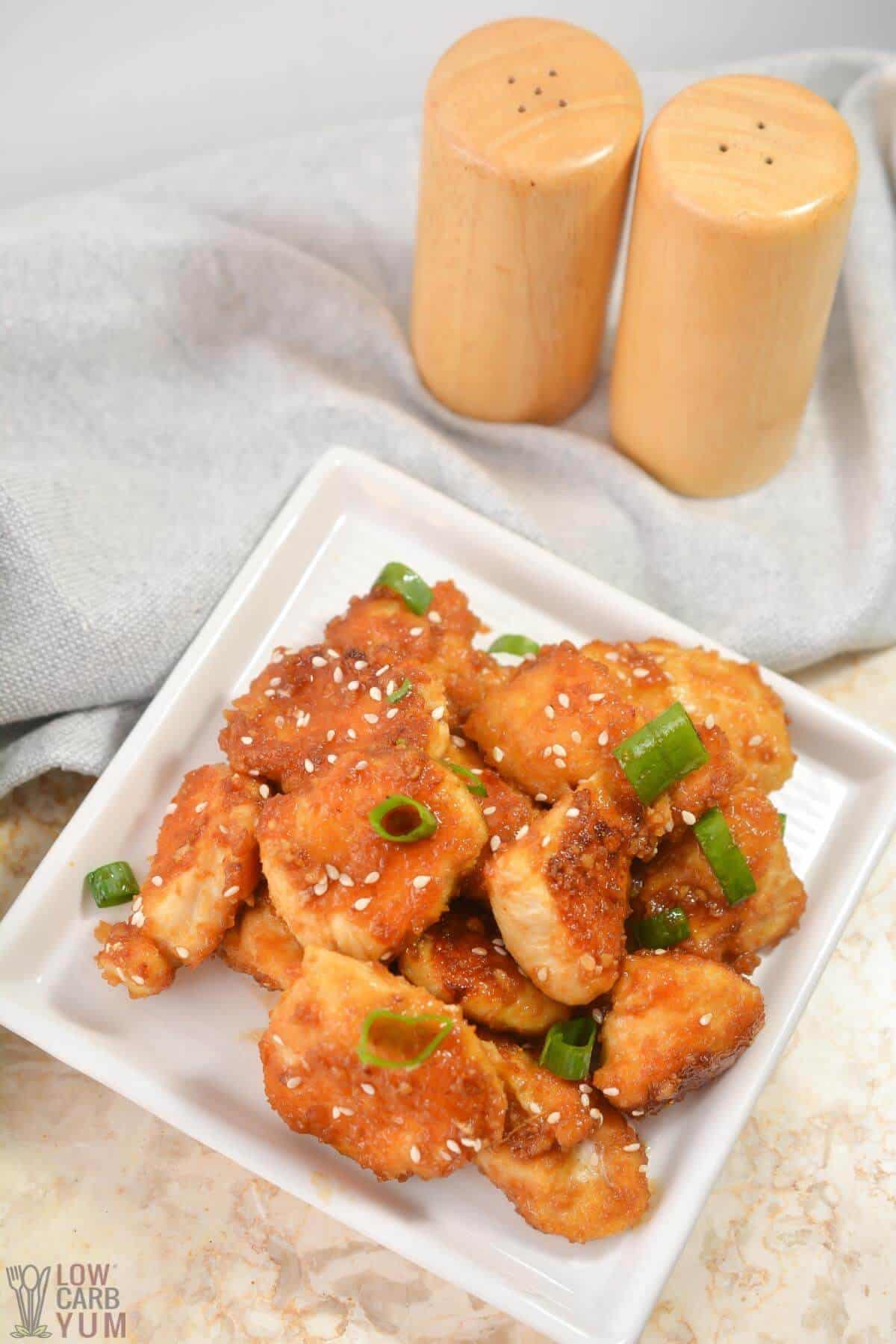 tall image of keto orange chicken on square white plate with salt and pepper shakers