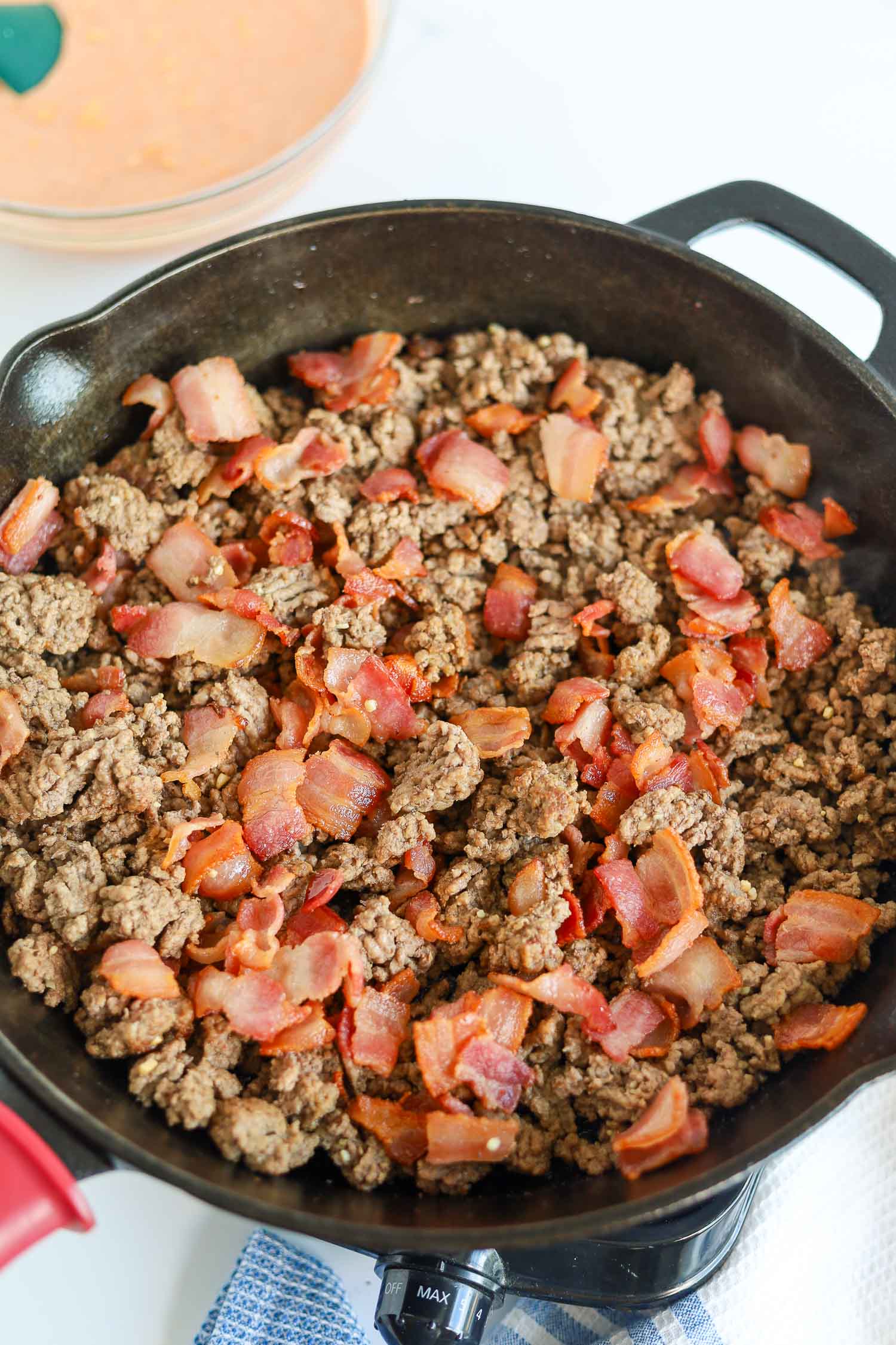 mixing cooked ground beef and crispy bacon bits in a cast iron