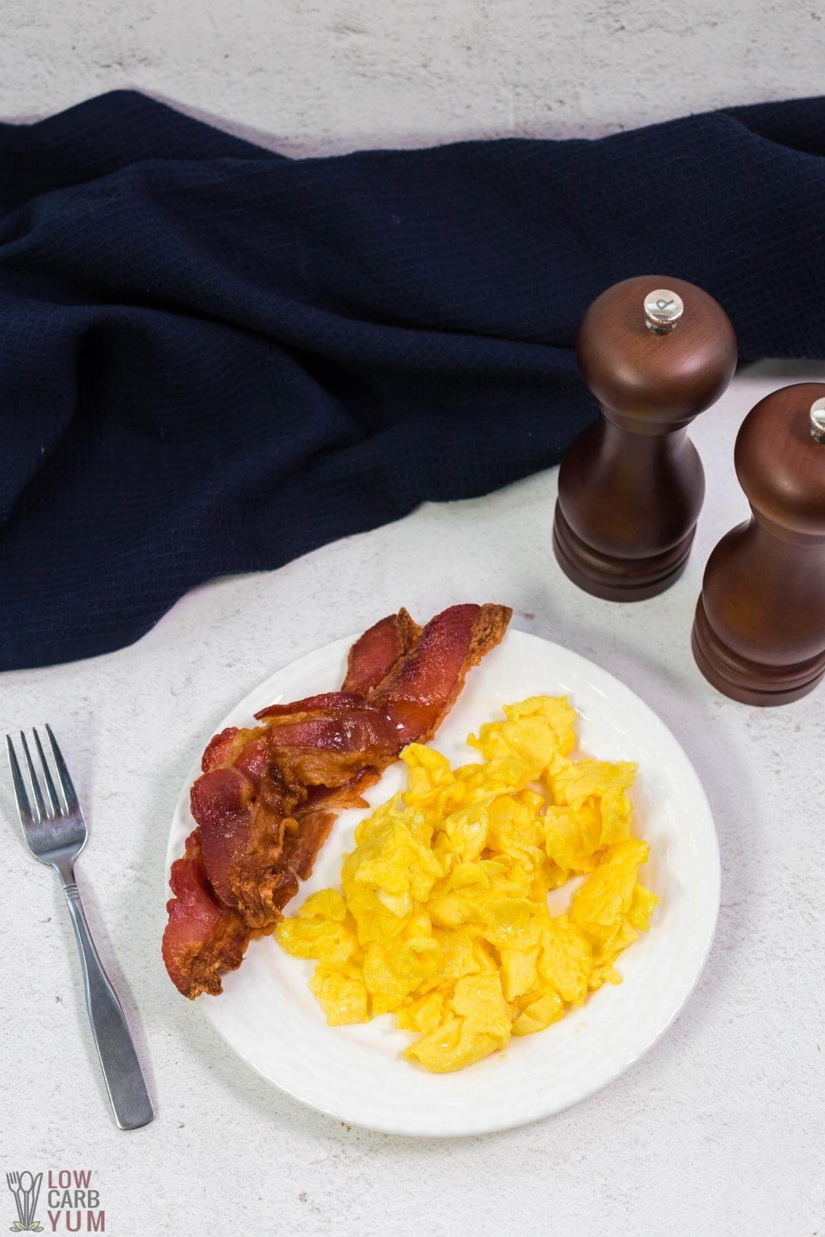 serving scrambled eggs on white plate with bacon salt and pepper