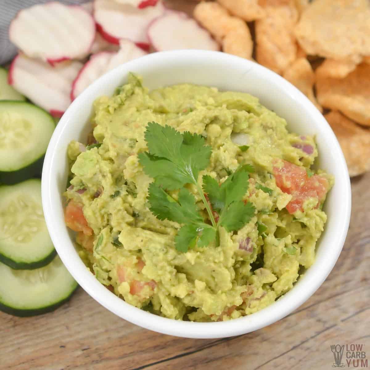 guacamole in white bowl with vegetables and pork rinds.