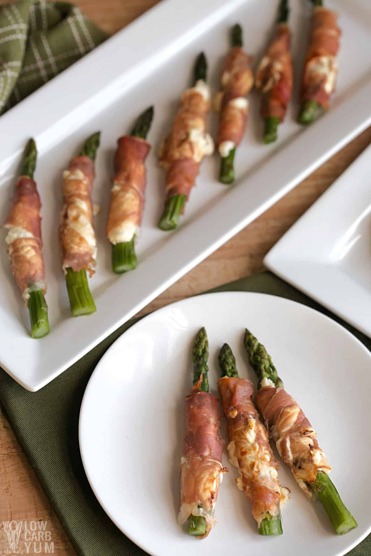 keto prosciutto wrapped asparagus is lined up on white plates.