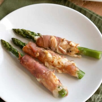 prosciutto wrapped asparagus on round white plate.