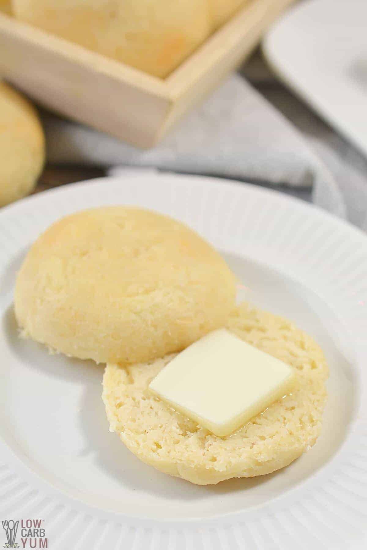 sliced dinner roll on white plate with pat of butter.