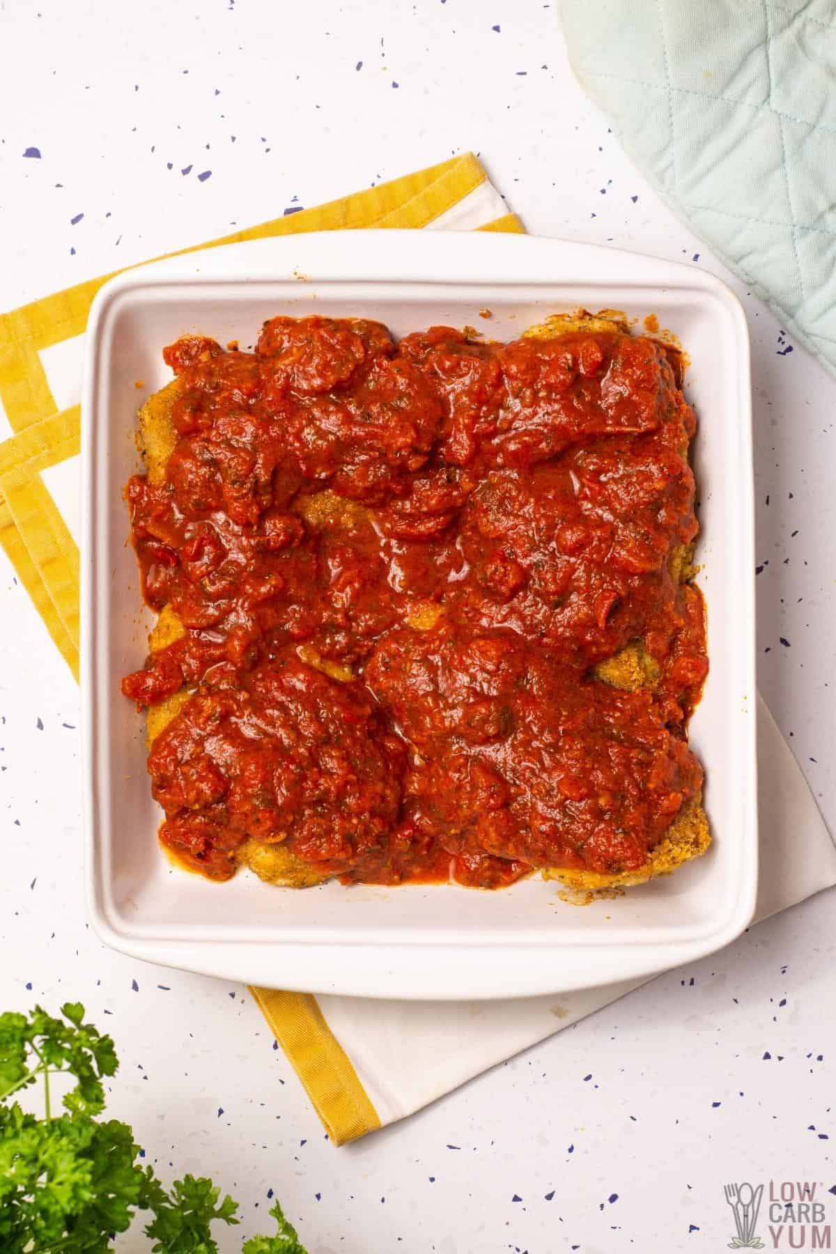 chicken topped with marinara sauce in square baking pan.