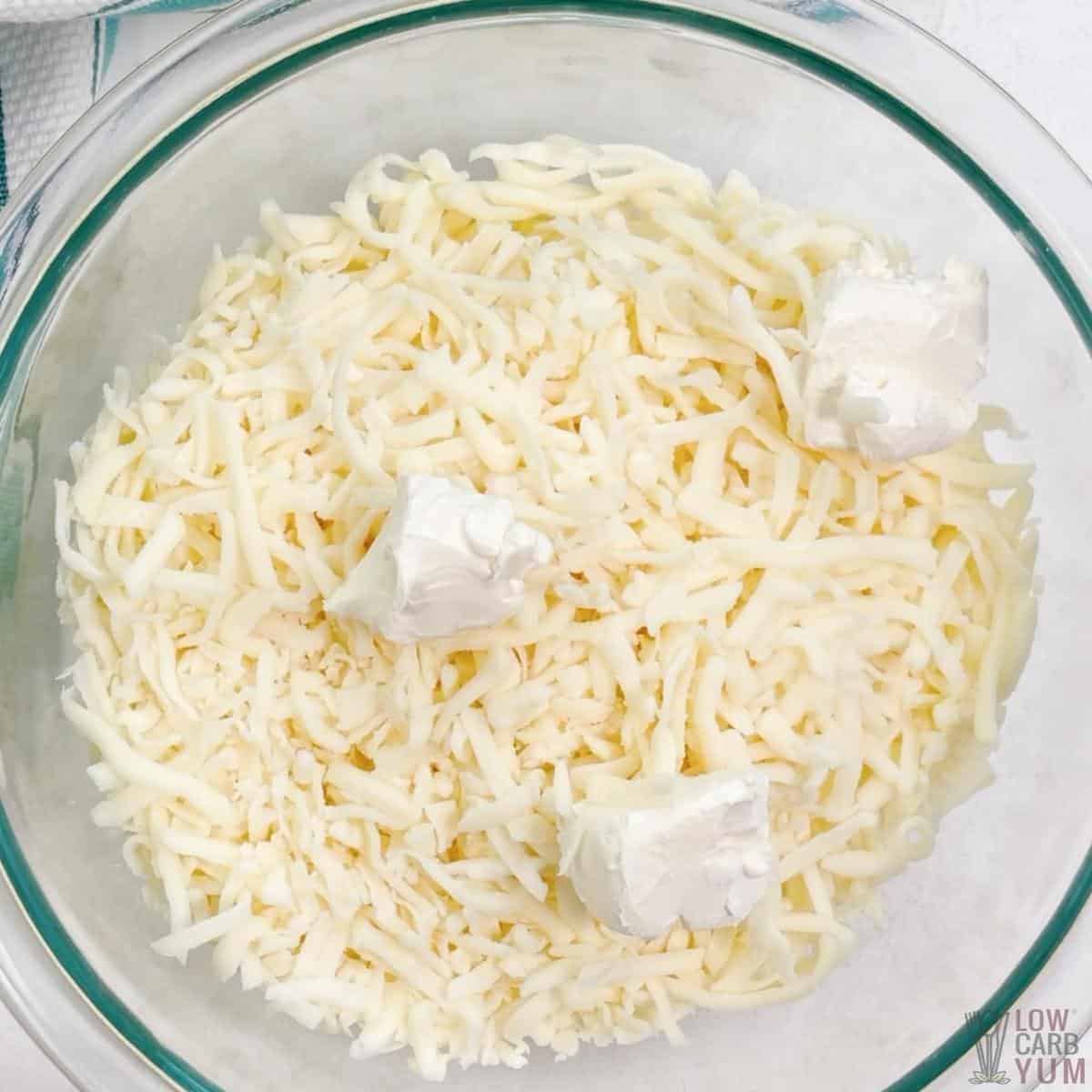shredded mozzarella cheese and cream cheese cubes in glass mixing bowl.