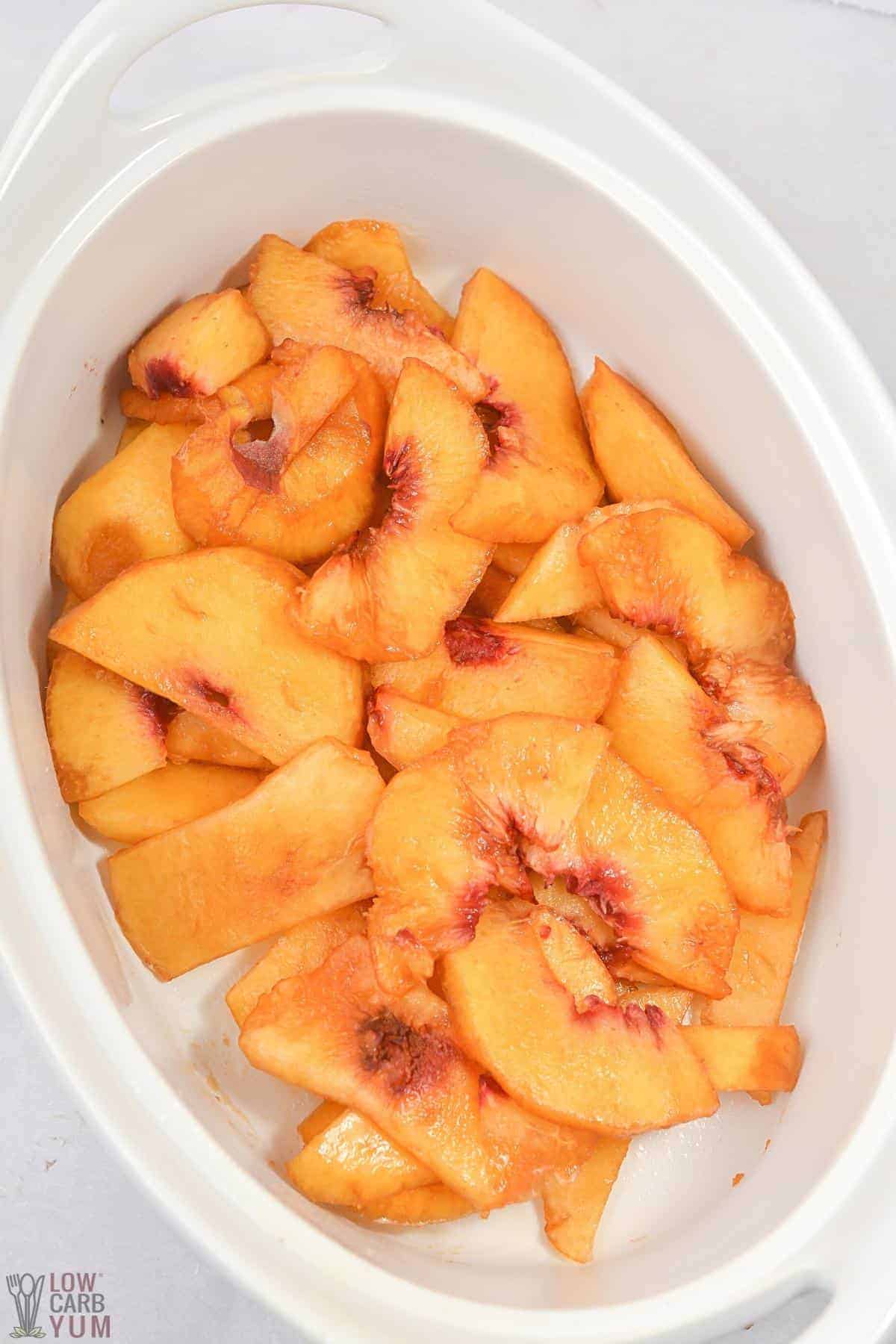 sliced skinned fresh peaches in white oval baking dish.