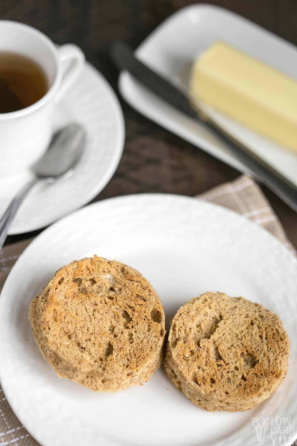 low carb english muffin sliced on white plate with butter and tea.