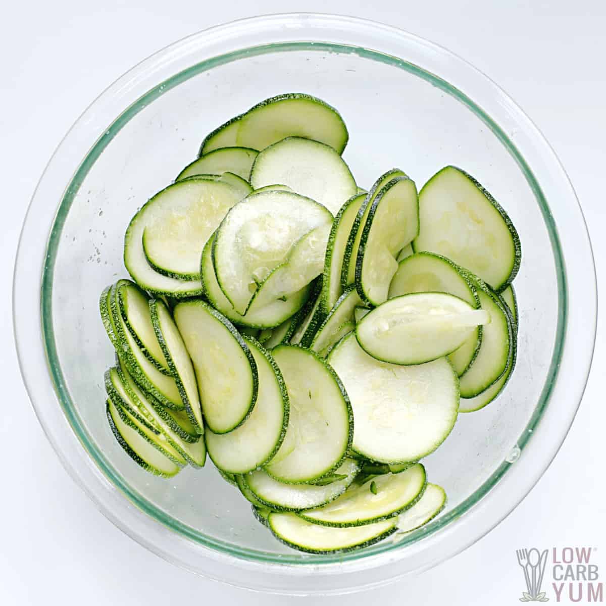 salted and oiled zucchini slices in glass mixing bowl.