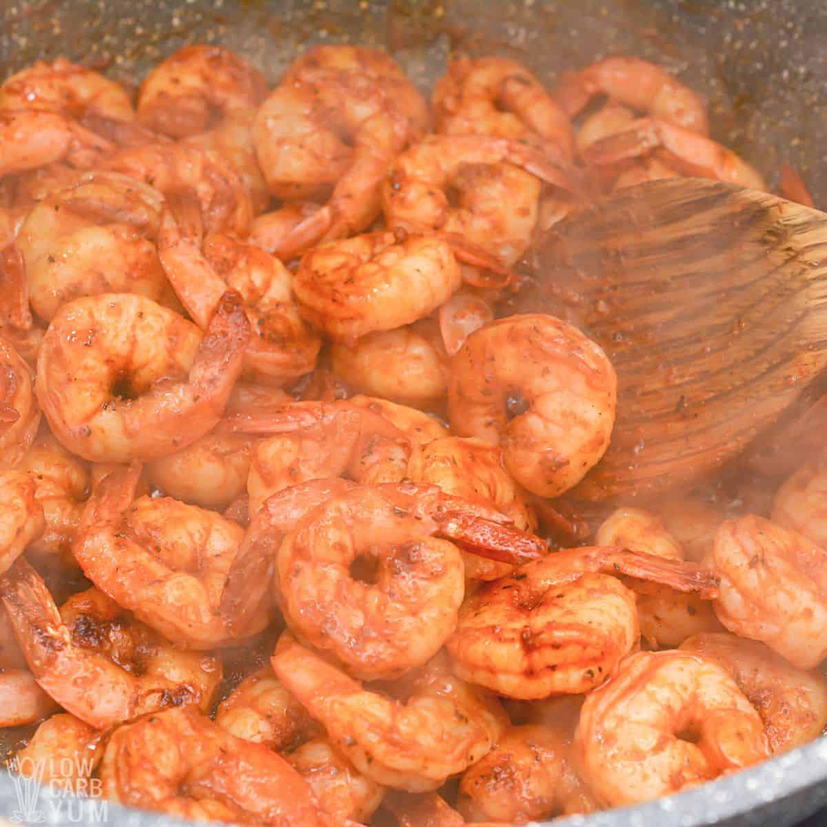 sautéing prawns in skillet with wooden spoon.