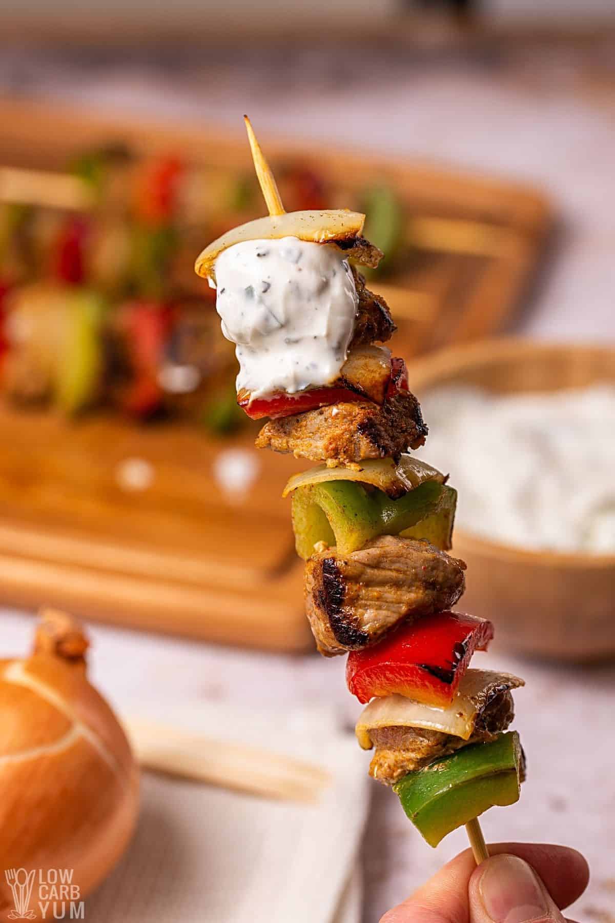 closeup of Greek meat and veggie skewers with sauce.