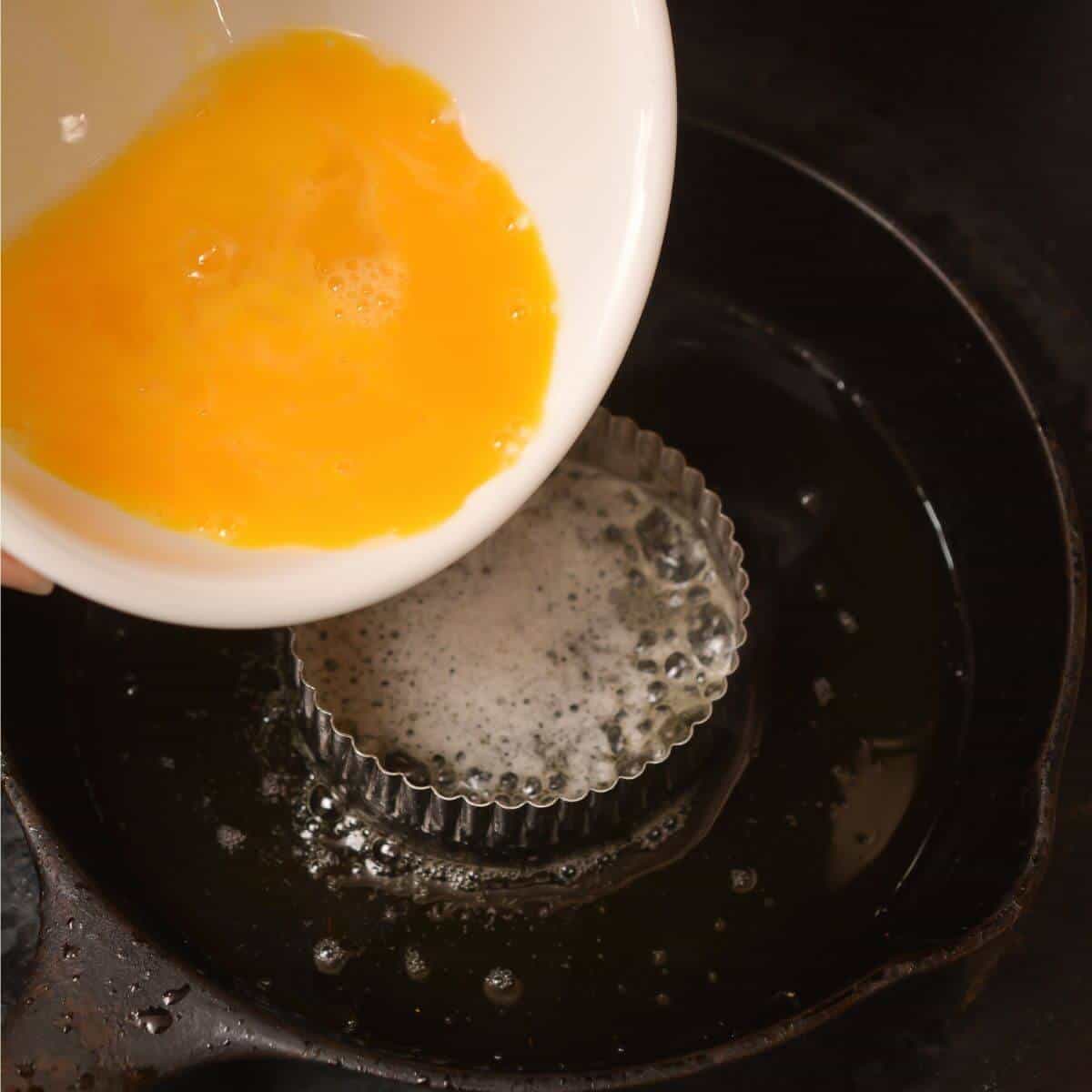 pouring beaten egg into buttered ring in iron skillet.