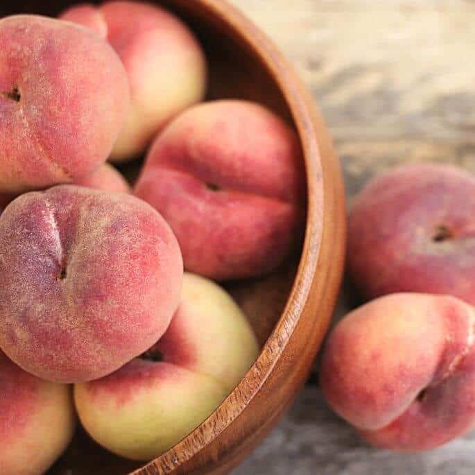 bowl of peaches with two on side.