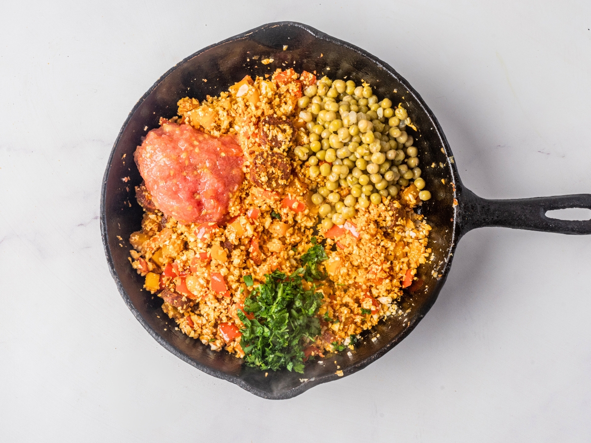 adding tomato sauce and green peas in cast iron skillet