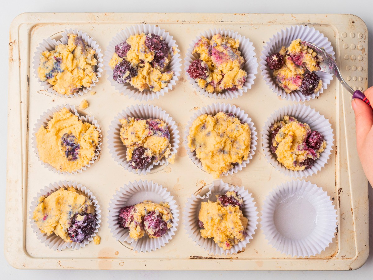 adding blackberry muffin batter to cupcake lined muffin tin