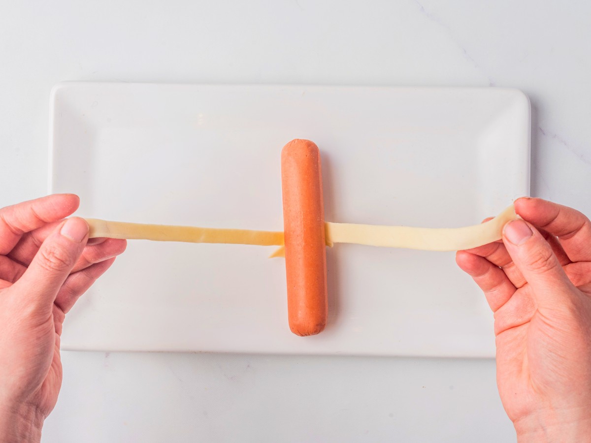 using a slice of pastry dough to wrap hot dog. 