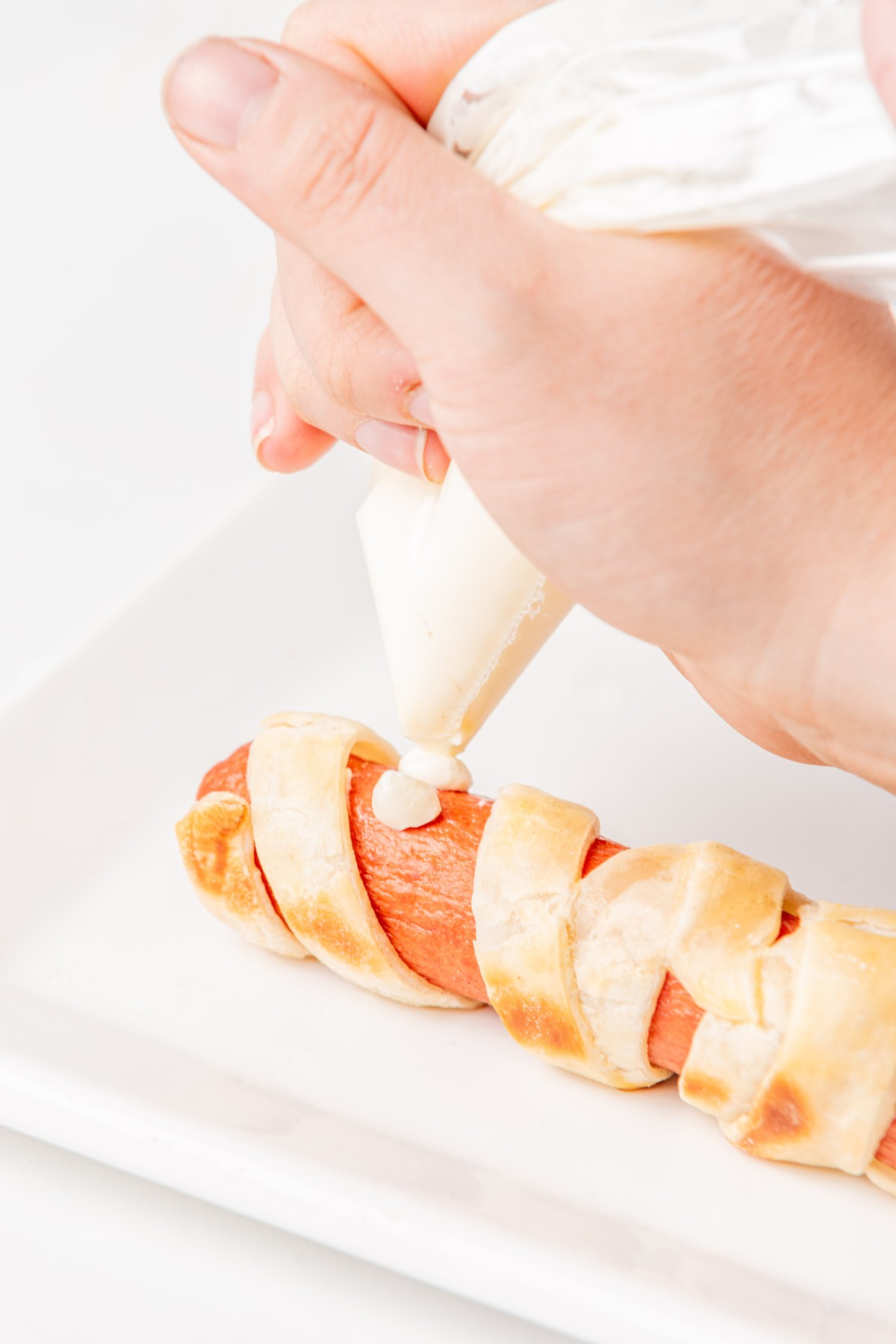 piping cream cheese eyes onto hot dog. 