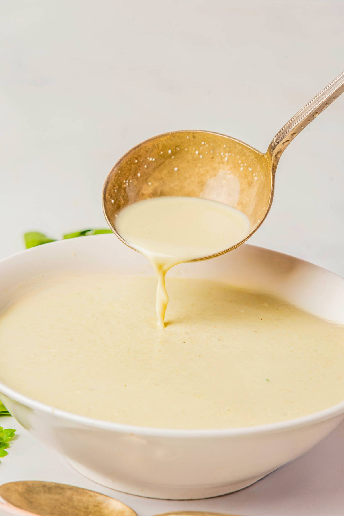 Pouring cream of celery soup in a white bowl