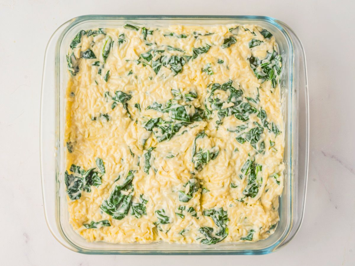 pouring creamy spinach dip into baking dish. 