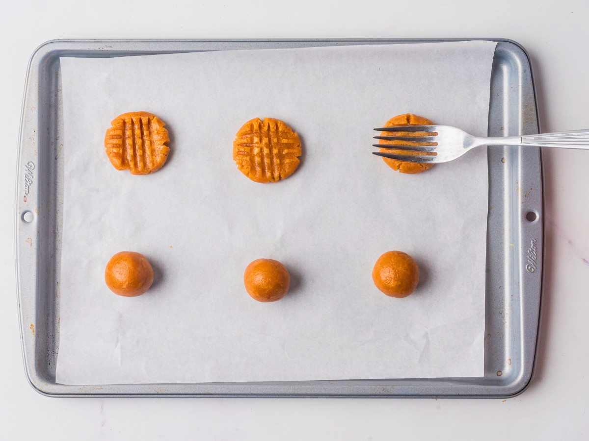 Using a fork to press on a criss cross pattern to the low carb peanut butter cookies.