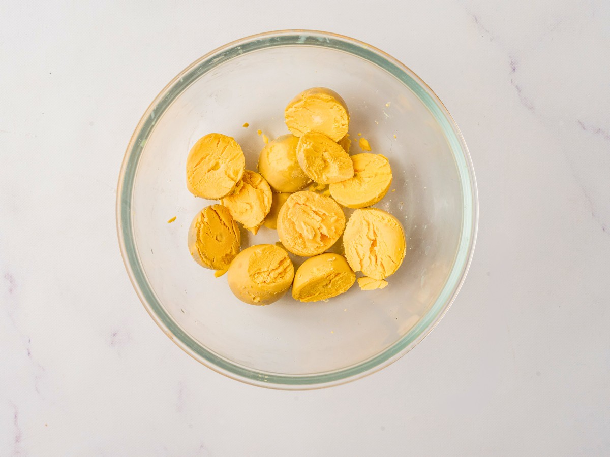 scooping out egg yolks into a glass bowl.