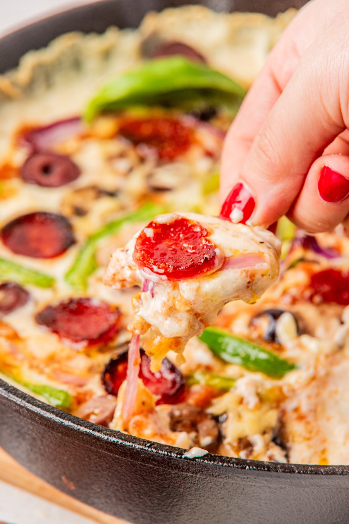 close-up shot of hand holding a chip with some pizza dip on it in front of the pan with the rest of the dip in it.