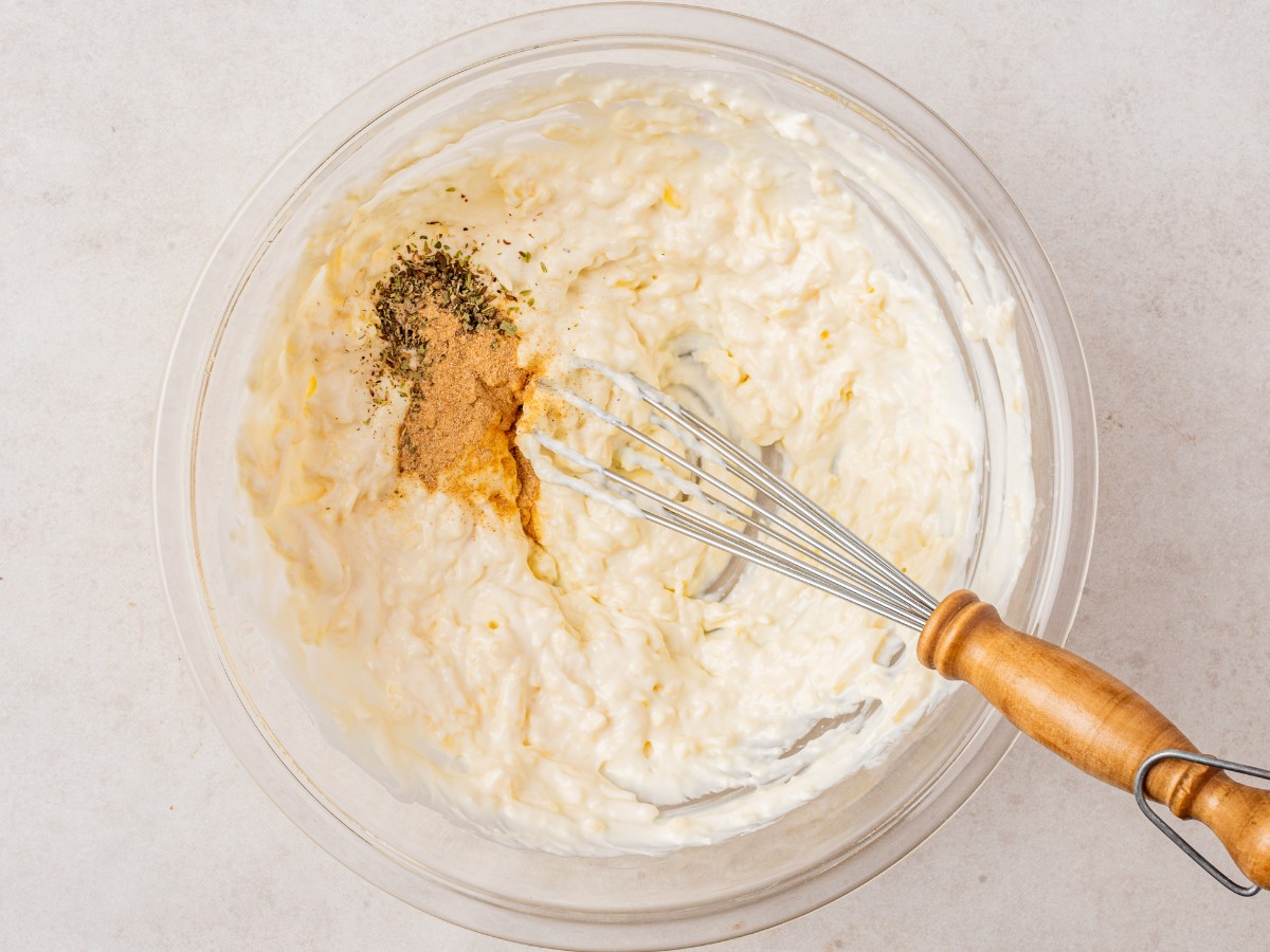 overhead shot showing seasonings added to the dip mixture in a glass bowl with a whisk.