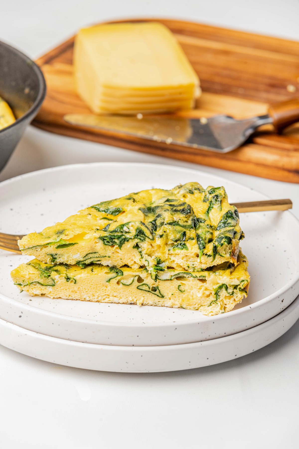 2 slices of cheesy spinach frittata on a white plate with a fork. 