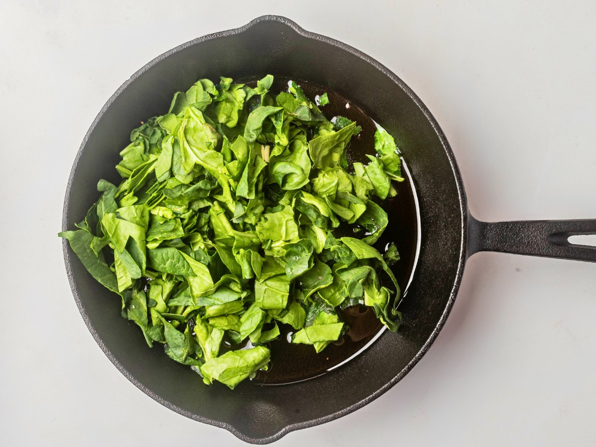 adding raw spinach to a pan