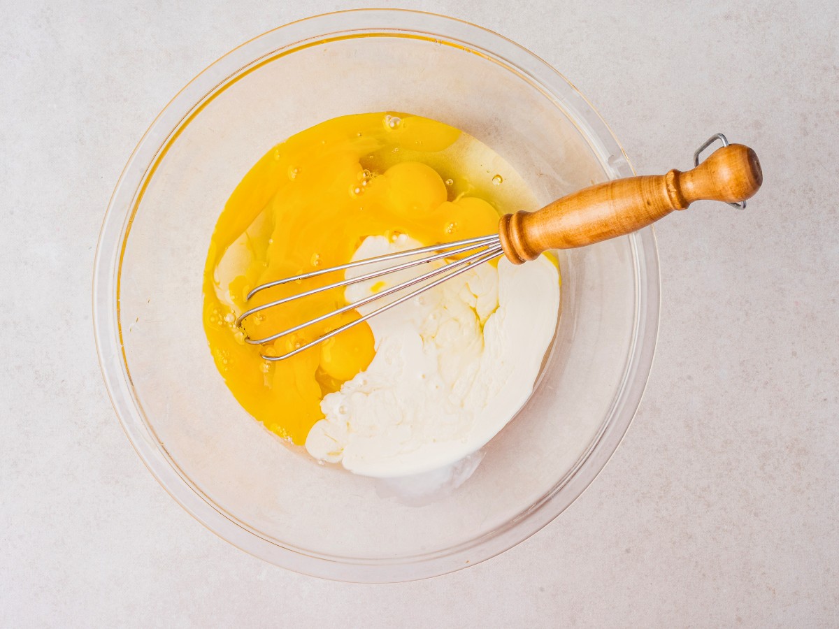 overhead shot of eggs and heavy cream in a mixing bowl with a whisk.